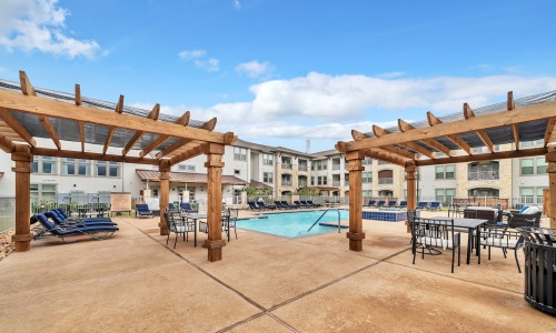 a swimming pool with a deck, tables and chairs